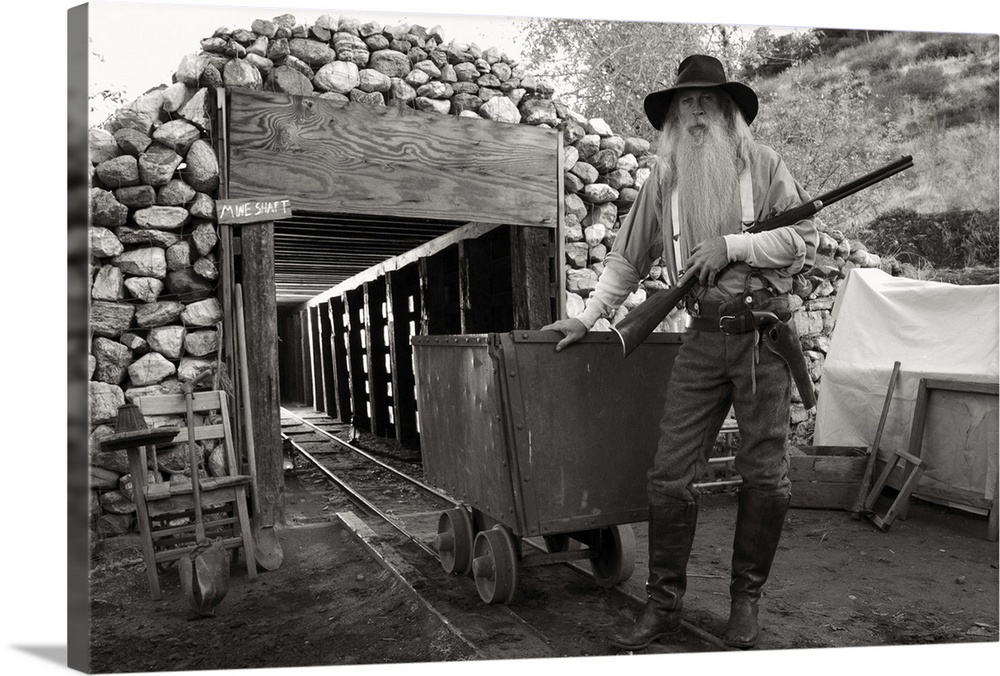 Old bearded man, a gold digger in front of a mine with a gun