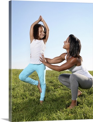A mom helps her five-year-old girl with a yoga pose