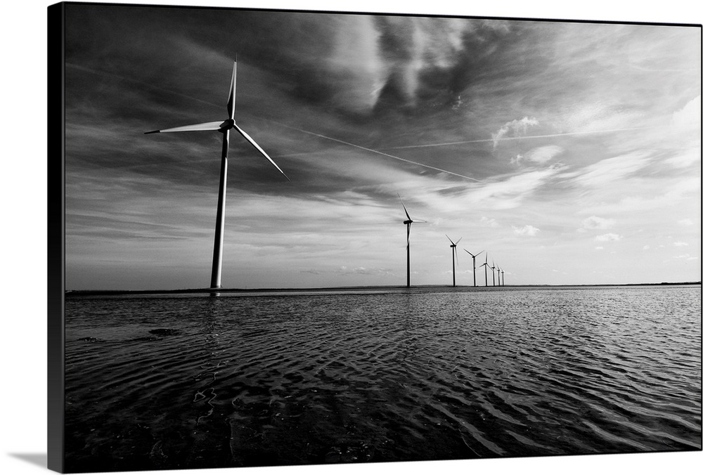 A row of windmills in the sea, in the water with a dramatic sky and dramatic clouds overhead.Black and white image.