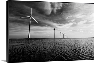 A row of windmills in the sea, in the water with a dramatic sky and clouds overhead