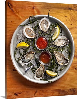 A selection of raw oysters arranged on a large platter with ice and spicy sauces