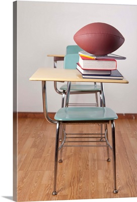 A student desk with a football sitting on a pile of school books.