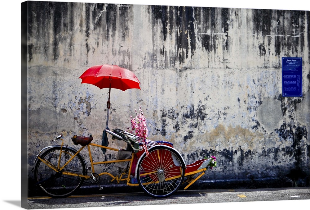 A traditional penang trishaw sits in front of an old weathered wall