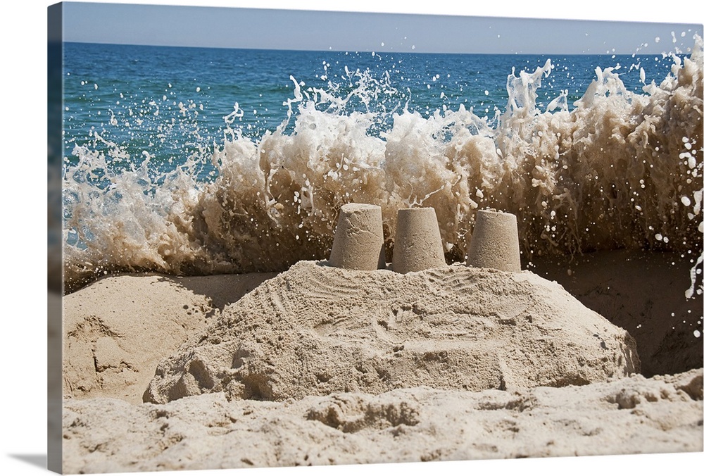 A large wave is captured just before crashing over and destroying a sandcastle. The sandcastle has three towers and a larg...