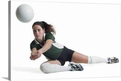 A young female volleyball player dives to the ground to hit a ball