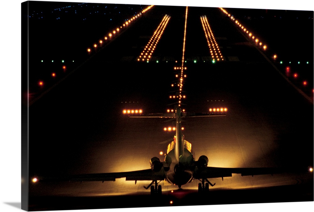 Giant photograph shows a small aircraft stationed at the end of a brightly lit airstrip at nighttime.