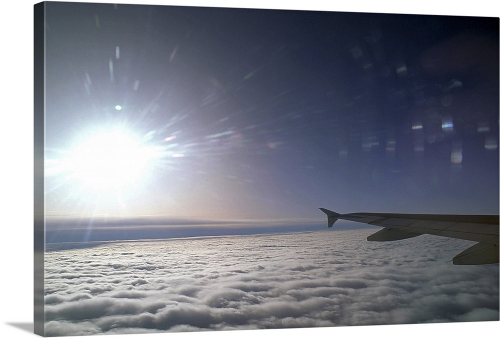 Airplane wing and sun above clouds