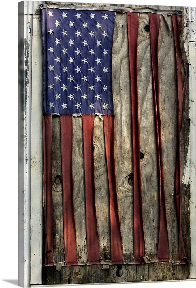 A vertical photograph of a flag nailed to a board that has become so distressed and weather beaten that the white stripes ...