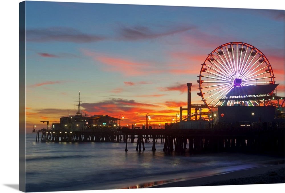 Large artwork of a beach pier during sunset skies with the rides lit up and ocean waves calmly crashing.