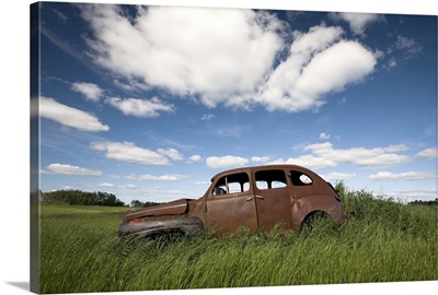 An abandoned classic car in a prairie field