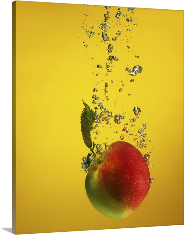 An apple splashed into water, creating bubblessplash. on yellow backdrop