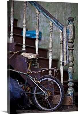an old staircase with paint peeling provides support for a childs bicycle