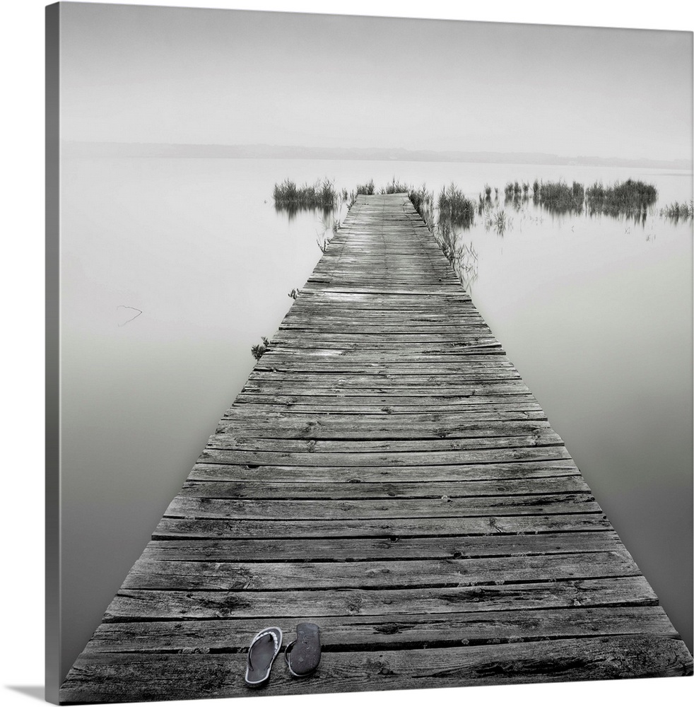 An old wooden jetty on a very calm lake. A pair of shoes are also lying on the jetty.