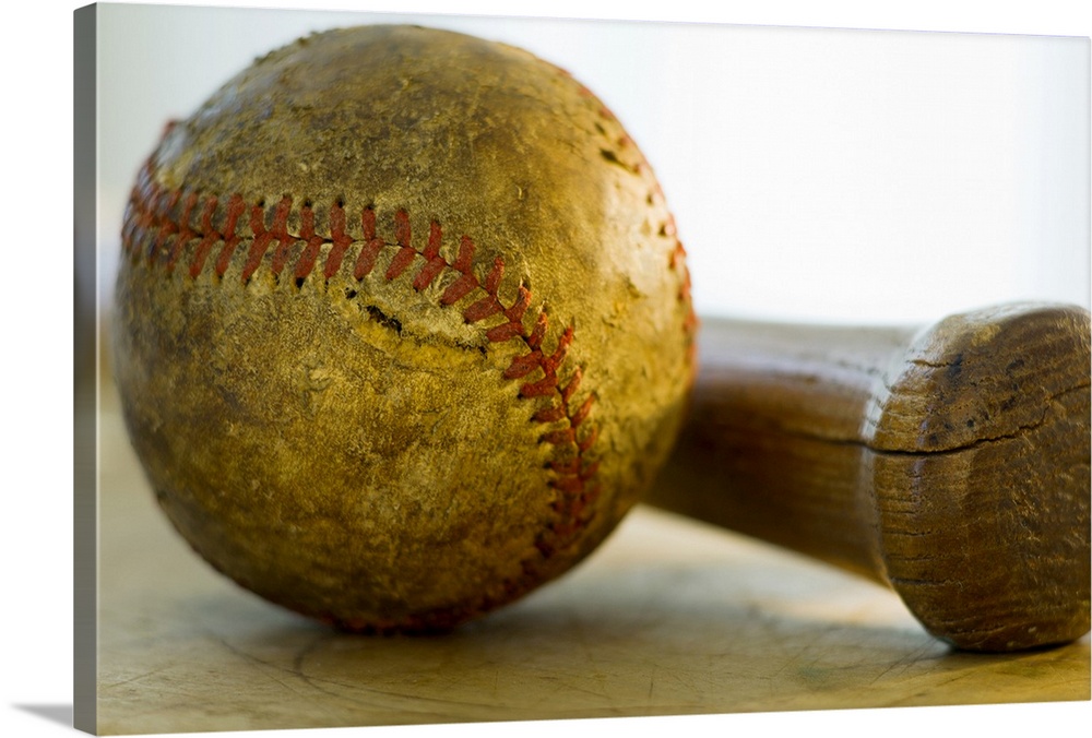 Huge photograph focuses on a stitched ball of worn cowhide sitting next to a wooden hitting instrument on a table.  Both o...