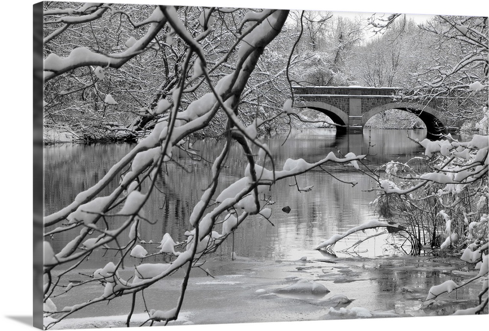 Winter scene of arch bridge over partially frozen river seen trough snow covered branches.