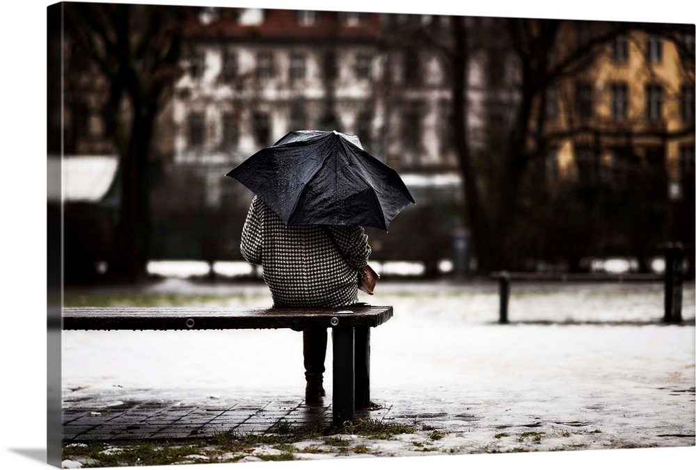 a woman with umbrella sitting on a parkbench on a rainy day in the city of Berlin