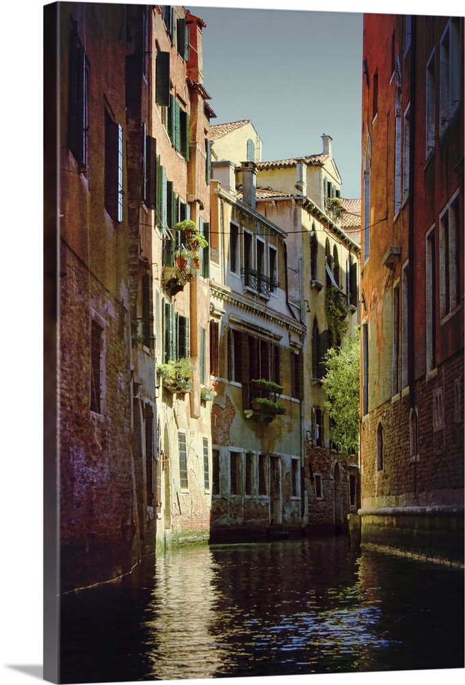 A pretty back street canal in Venice Italy shows exposed brick buildings and shuttered windows.