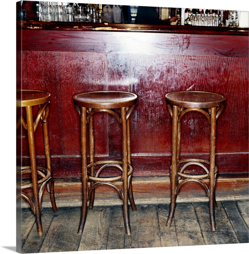 Three tall stools are photographed sitting in front of an empty bar.