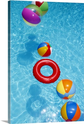 Beachballs blowing in wind in sparkling blue swimming pool.