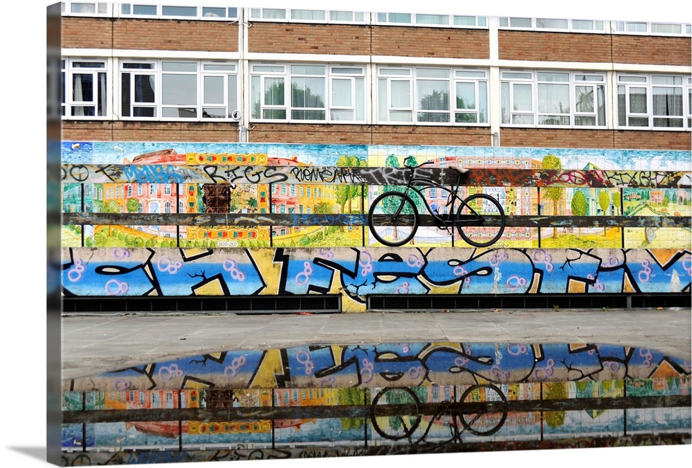 Bike chained to a graffitied fence and wall on a housing estate reflected in a puddle, East London, UK