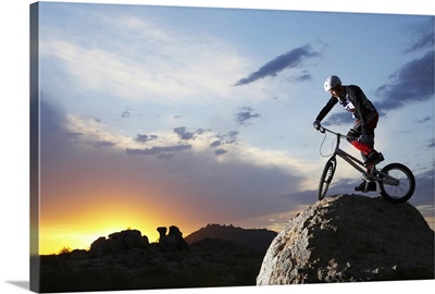 Bike rider balancing on rock boulder, side view