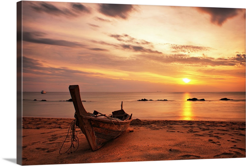 A beautiful picture taken of a wooden boat sitting on the beach as the sun begins to set in the distance.