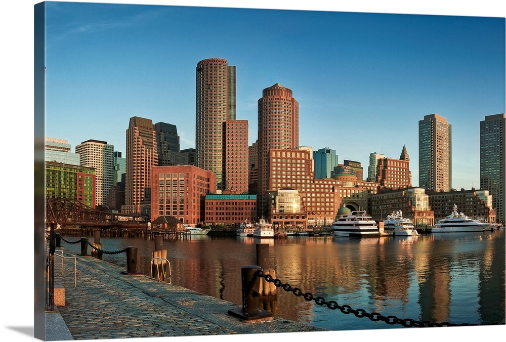 This wall art is a horizontal photograph taken from a harbor dock that shows several skyscrapers and big yachts floating o...