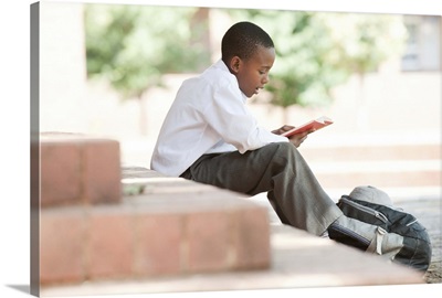 Boy reading on steps outside school