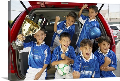 Boys (7-11) football team in car boot, holding trophy, smiling