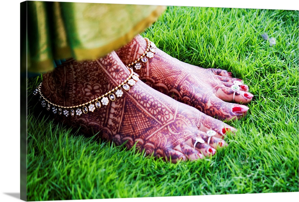 Brides feet with mehndi standing on green grass.