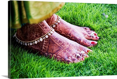Bride's feet with mehndi standing on green grass.