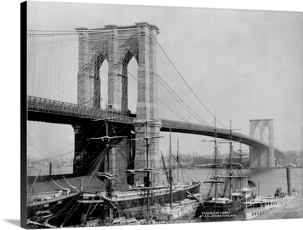 Sailing ships rest in port below the Brooklyn Bridge. The Brooklyn Bridge, designed by John A. Roebling, became the larges...