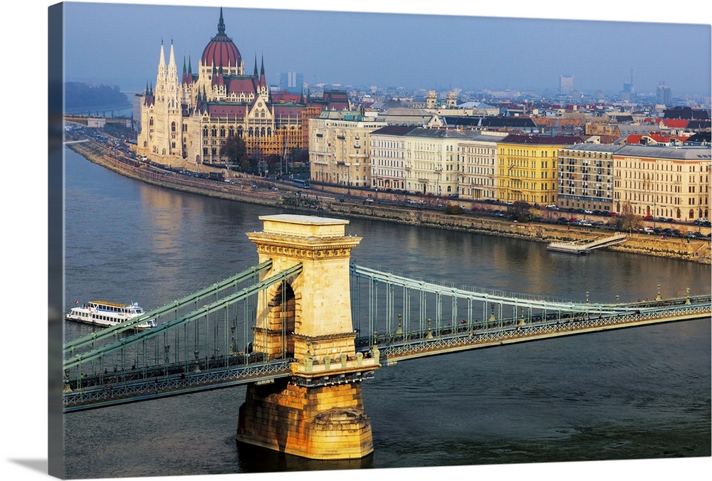 Warm sunlight spotlights the Chain Bridge and the Hungarian Parliament Building against a blue sky and Danube River.