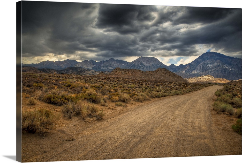 High desert dirt road leading to the cloudy High Sierra mountains