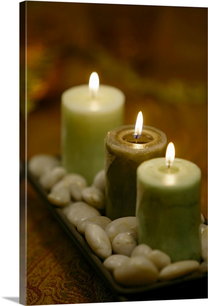 Relaxing photograph of three lit candles resting in a shallow dish of round, polished pebbles.