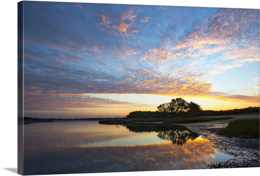 sunrise on a bay on Cape Cod, Massachusetts, with the silhouette of a tree and reflection of the tree and beautiful sky in...