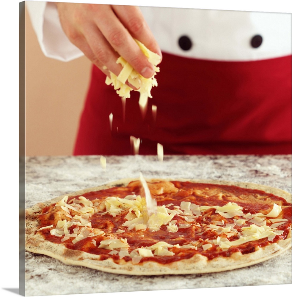 Close-up of a chef preparing a pizza. Hands sprinkling cheese on pizza topped with mozzarella and tomato sauce. Granite wo...