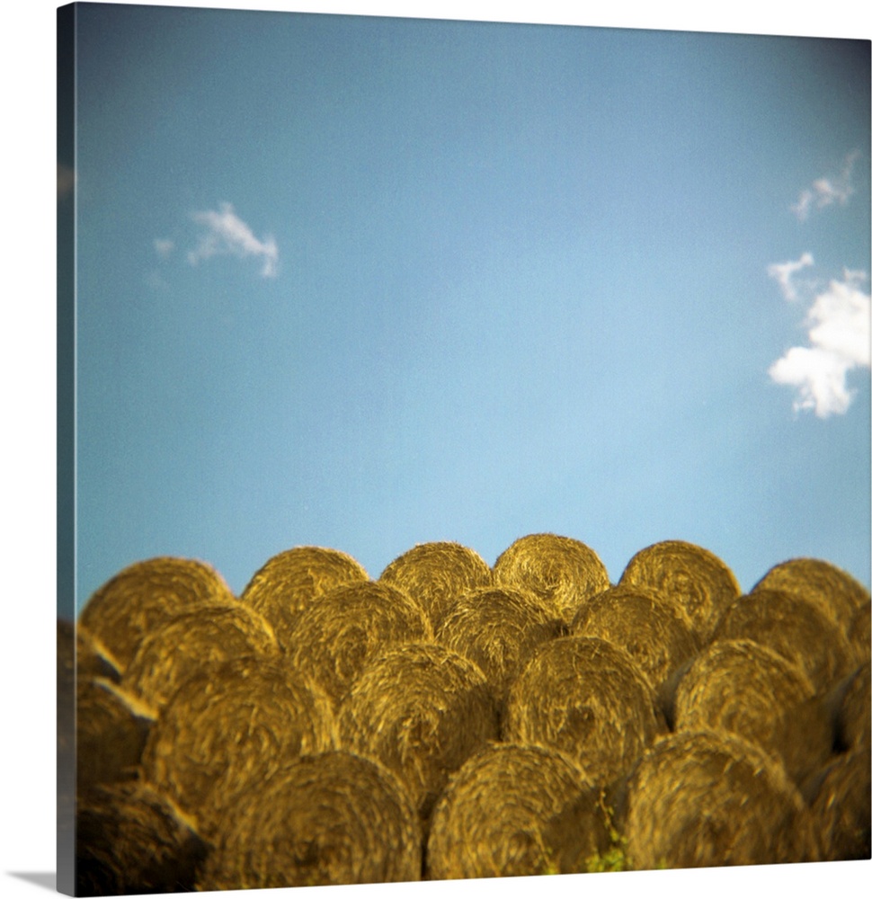circular hay bales against blue sky with small white clouds.