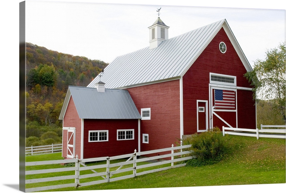 Classic New England farm with red barn and white fence. American flag on barn door. Vermont. USA