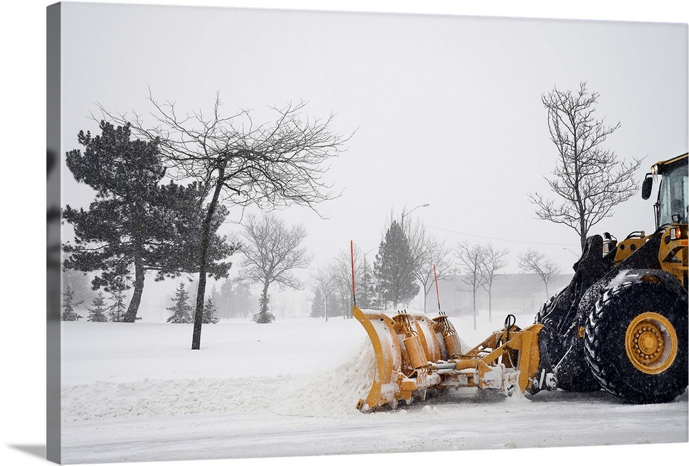 A snow plow / tractor clearing the snow on the roads from a winter storm.