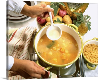 Close-up of a hand stirring a bowl of soup cooking on a stove