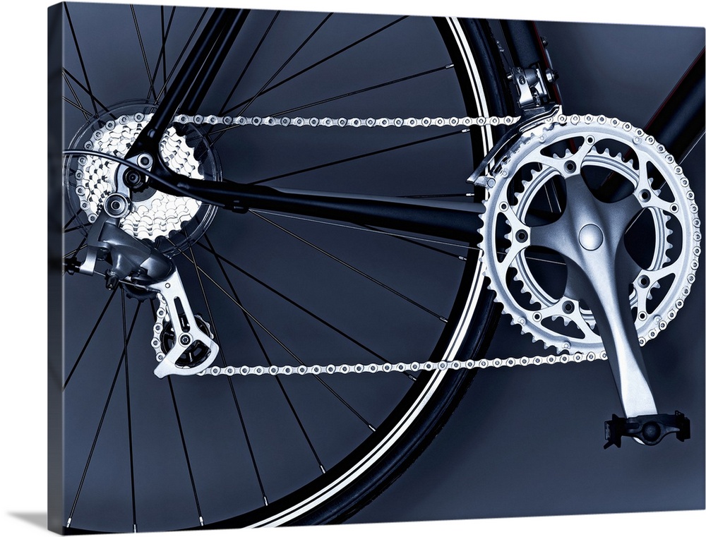Oversized, horizontal, close up photograph of part of the back wheel, the chain, gears and pedal of a black bicycle.