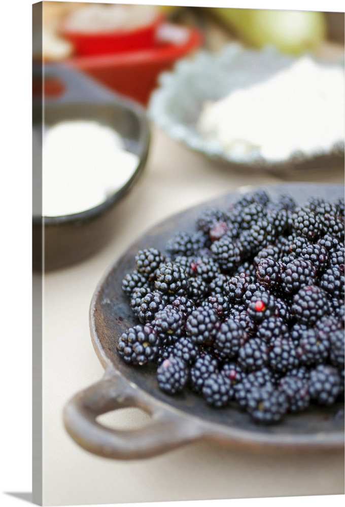 Close up of bowl of blackberries on a table with bowls of cheese and breads in the background.