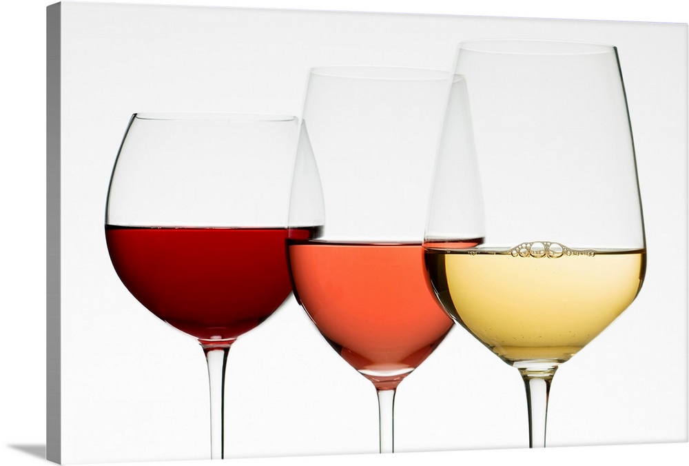 Three different wine glasses stand next to each other all filled with different types of wine.