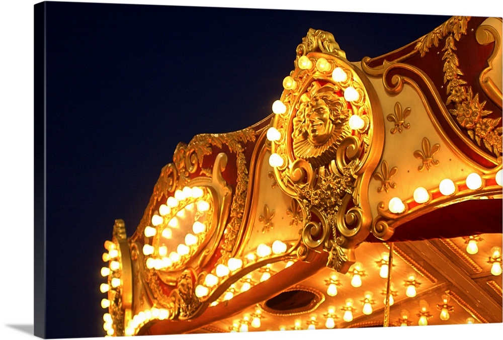 Close-up of the lights and ornate artwork on the top of a merry-go-round at a fair.