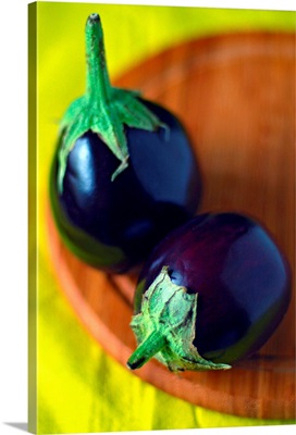 Close-up of two tiny round eggplants on round wooden chopping board