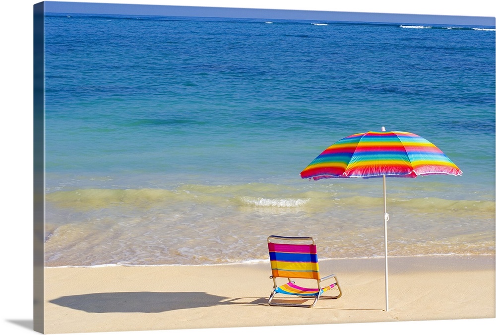 Colorful beach chair and umbrella on the shoreline of a tropical beach, calm waves washing ashore, turquoise water.