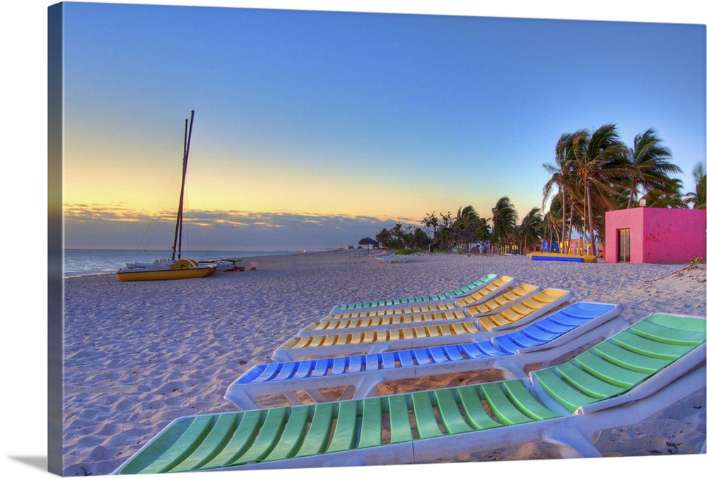Early morning image featuring colorful beach chairs, palm trees, and catamaran along white sand beach along Cubas northern...