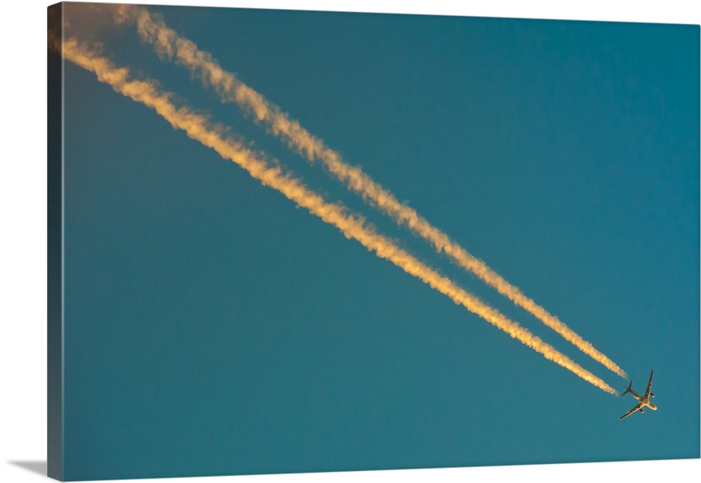 Long condensation trails in blue sky at sunset.
