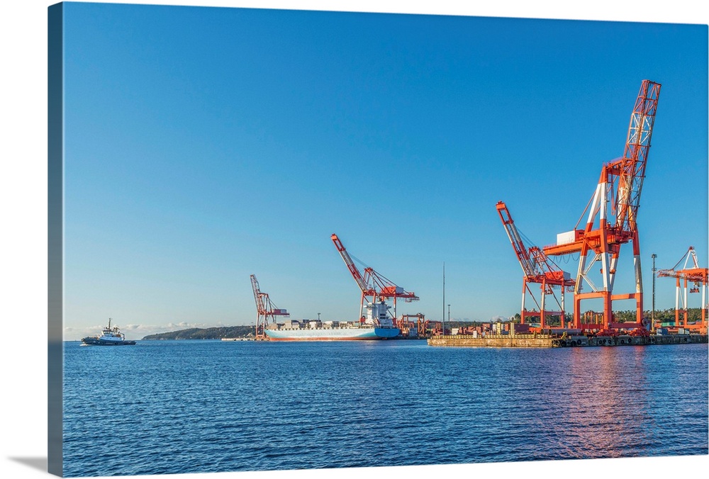 A container ship docked, preparing for cranes to unload its cargo. A tugboat is leaving the ship having done its job.